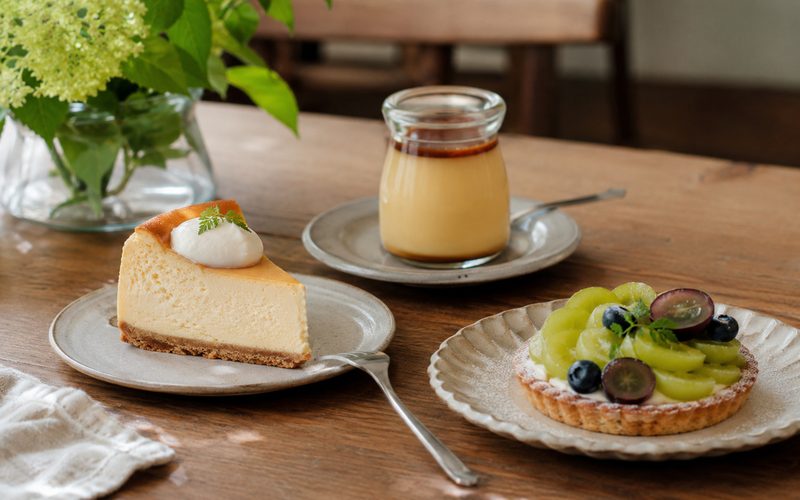 木のテーブルに並ぶ自家製のチーズケーキ・プリン・季節のタルト