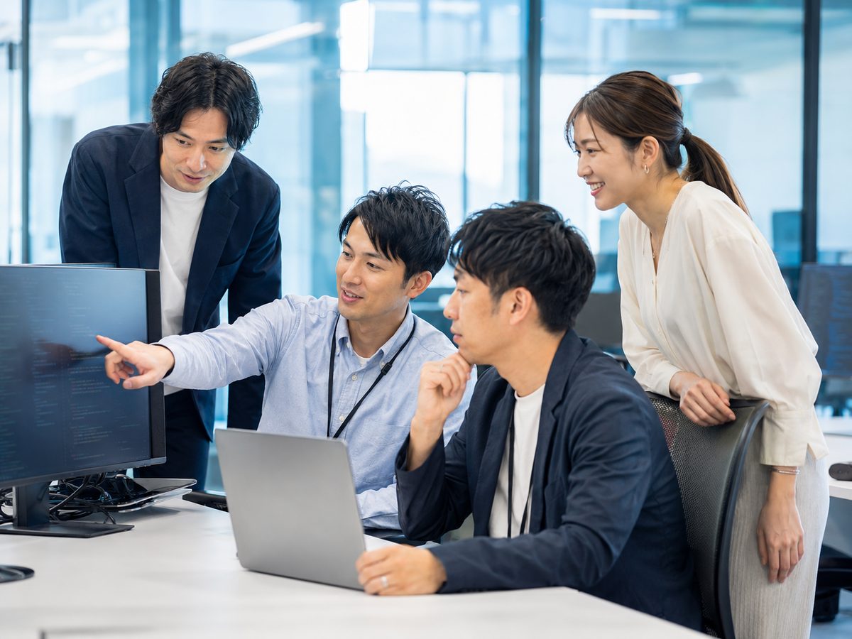 オフィスでモニターを囲みコードレビューを行う開発チーム